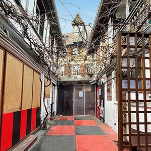 Photo de la cour du théâtre de la Choucrouterie : le sol est peint dans une alternance de damiers rouges et noirs. Sur la gauche, on voit l'entrée de la petite salle du théâtre et, au fond, l'entrée de la grande salle.